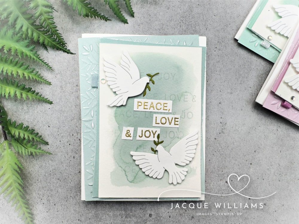 Handmade Christmas card featuring the Stampin’ Up! Peaceful Garden suite with two white die-cut doves holding olive branches. The card has a soft watercolor background in Pool Party with embossed leaves and the sentiment “Peace, Love & Joy.” Perfect DIY cardmaking idea for Christmas, weddings, or sympathy cards.