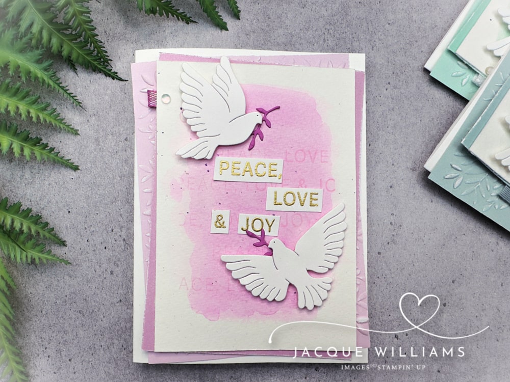 Handmade Christmas card featuring the Stampin’ Up! Peaceful Garden suite with two white die-cut doves holding olive branches. The card has a soft watercolor background in Pool Party with embossed leaves and the sentiment “Peace, Love & Joy.” Perfect DIY cardmaking idea for Christmas, weddings, or sympathy cards.