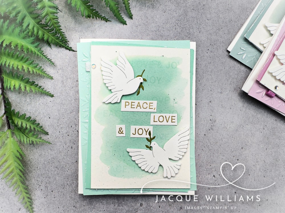 Handmade Christmas card featuring the Stampin’ Up! Peaceful Garden suite with two white die-cut doves holding olive branches. The card has a soft watercolor background in Pool Party with embossed leaves and the sentiment “Peace, Love & Joy.” Perfect DIY cardmaking idea for Christmas, weddings, or sympathy cards.
