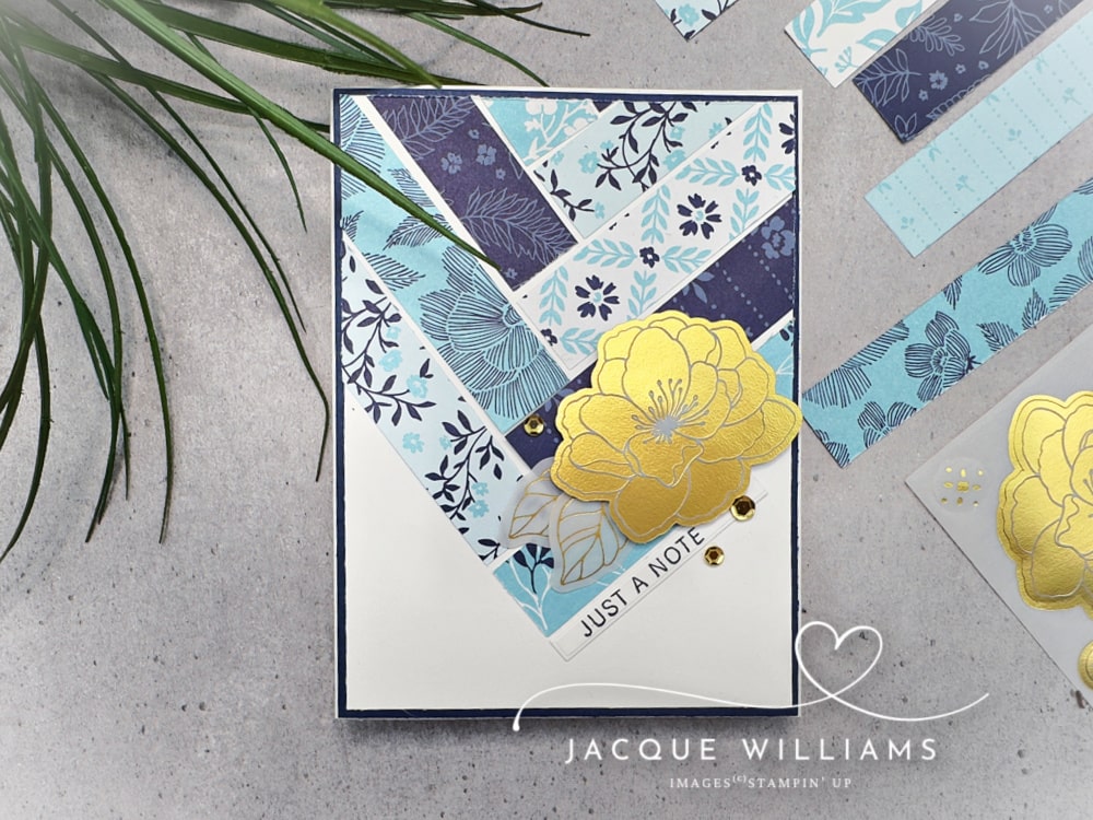 Handmade Stampin’ Up! card featuring the True Blue Designer Series Paper layered in a modern geometric layout, accented with a yellow floral die cut from the Beautifully Ornate Ephemera Pack. Clean and simple cardmaking design with navy, soft blue, and white tones, gold embellishments, and a “Just a Note” sentiment—ideal for everyday handmade cards and paper crafting inspiration.